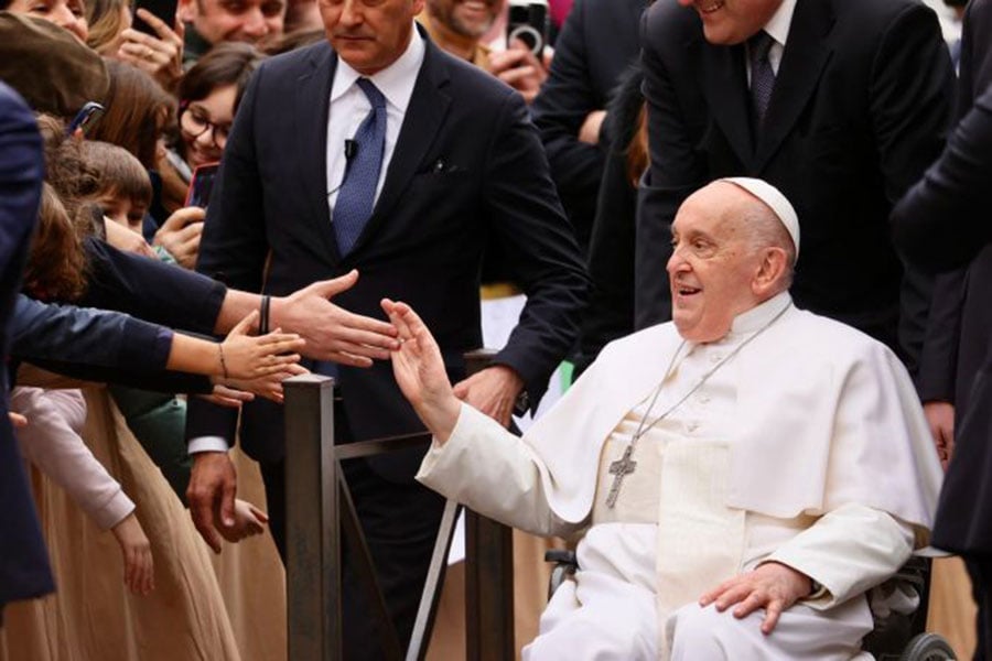 Pope Francis waves at a crowd while in a wheelchair