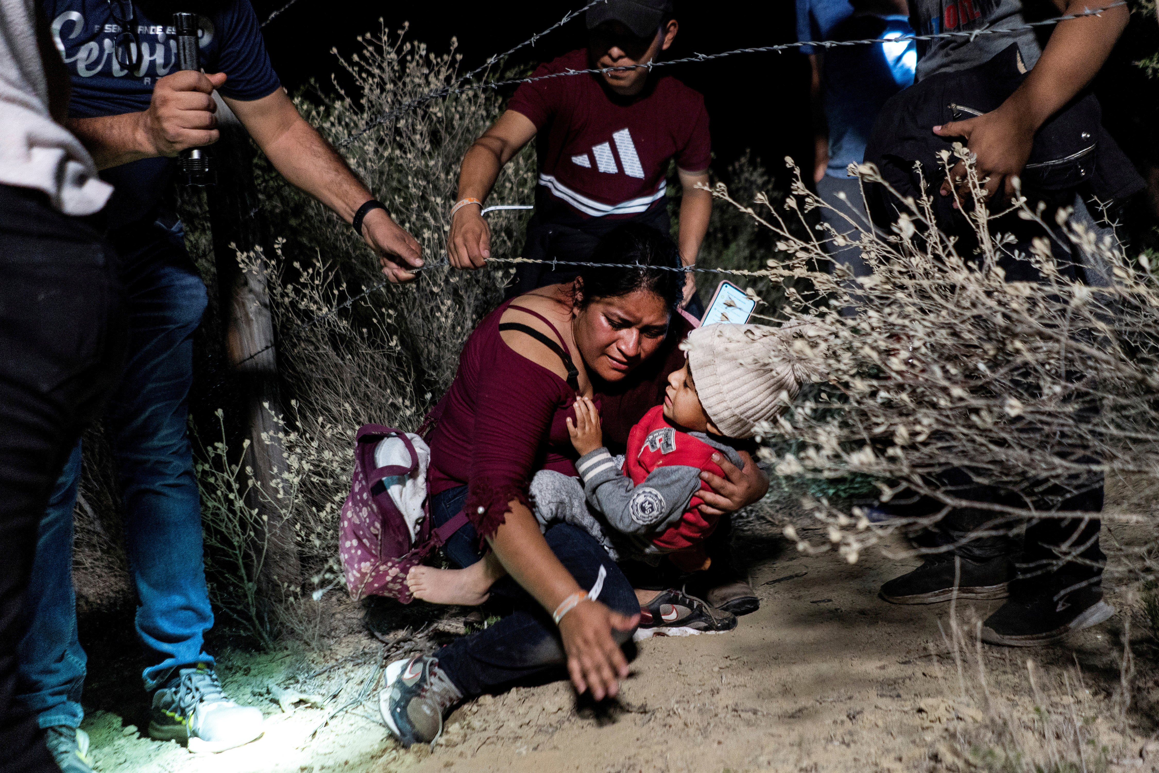 woman ducking under barbed wire at night with baby in her arms
