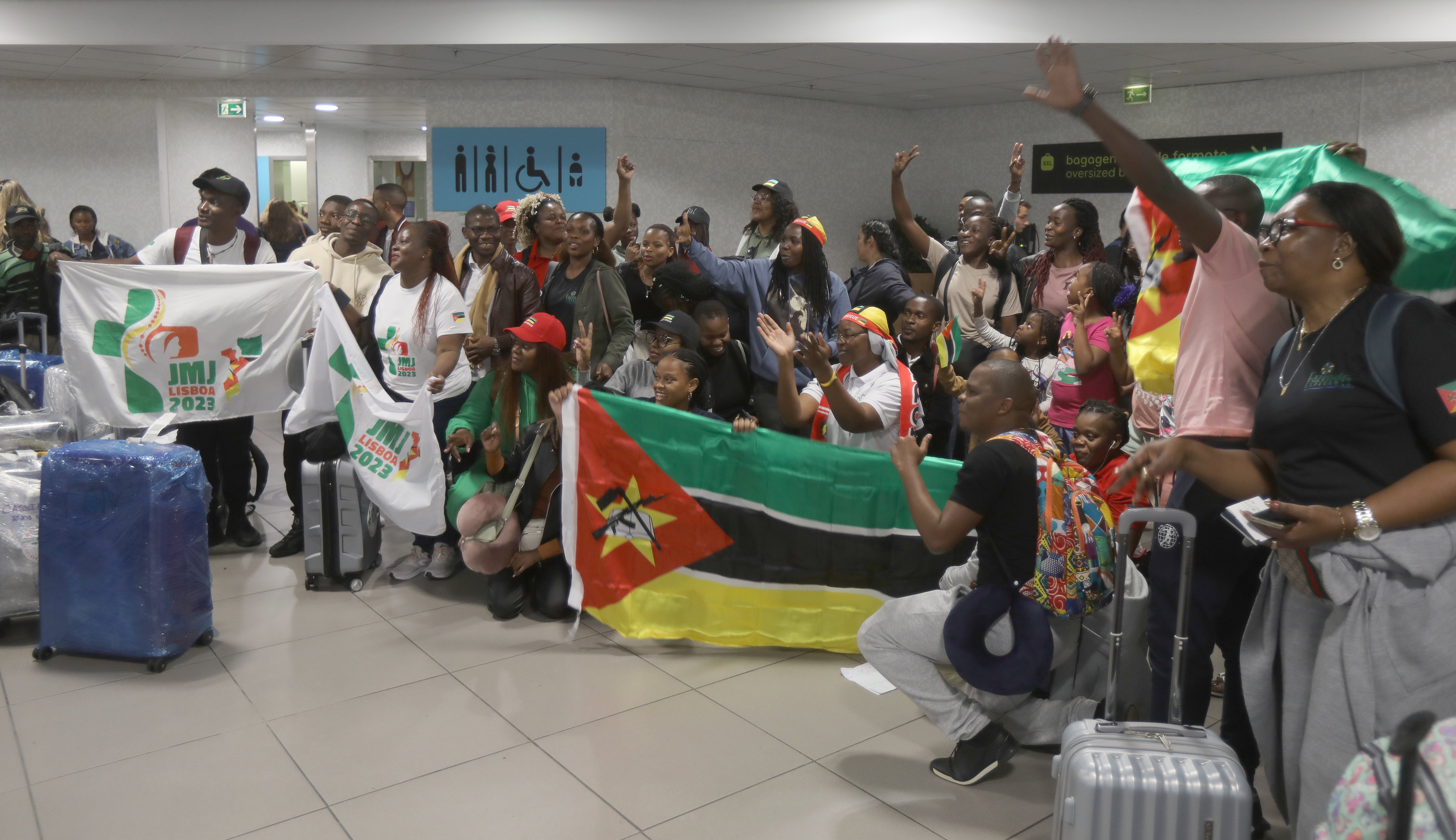 a group of pilgrims from Mozambique appear to be cheering for a picture in an airport hallway