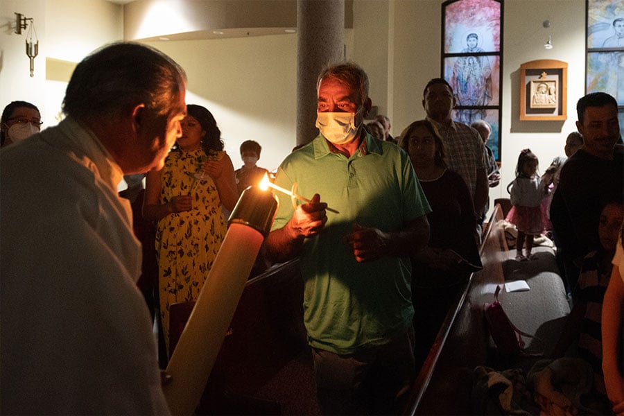 Deacon Angelo Lombardo, left, holds the paschal candle has he lights the candles of parishioners during the Easter Vigil Mass at Immaculate Conception Parish in Denton, on Saturday, April 16, 2022.