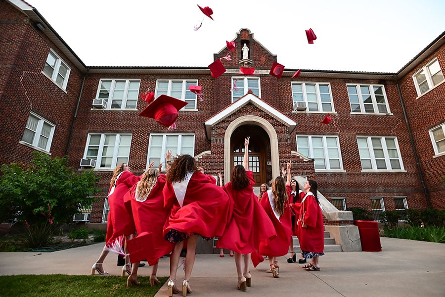 Graduates of Sacred Heart Catholic High School celebrate by throwing their graduation caps into the air.