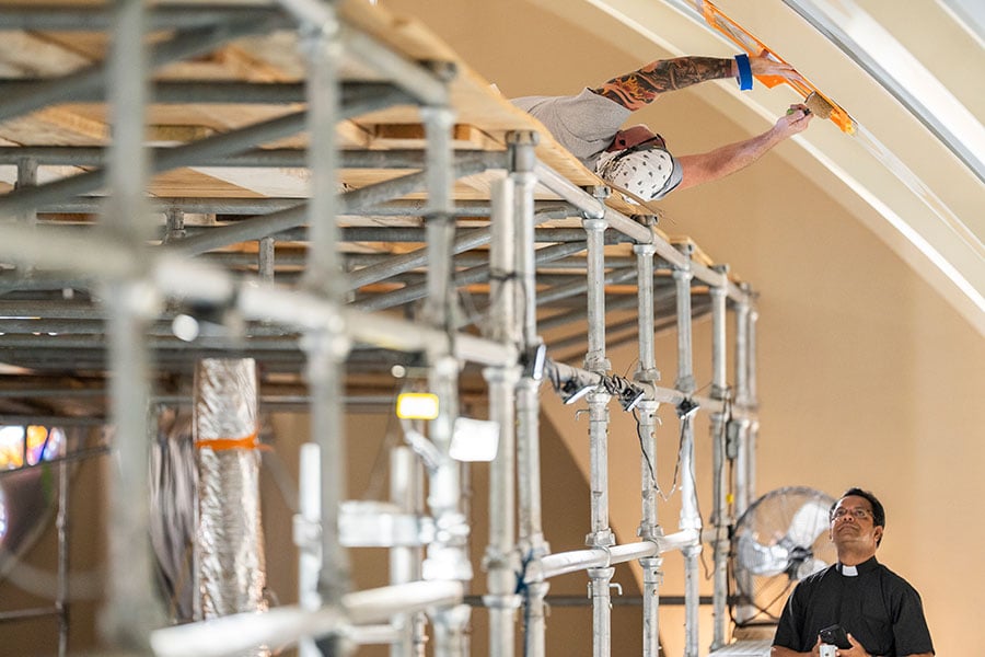 man paints ceiling while Fr. John watches