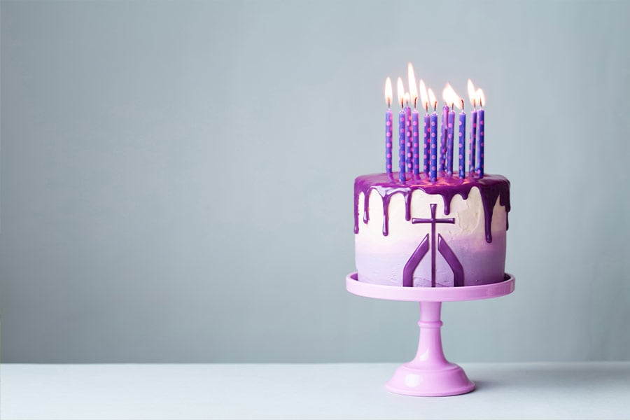 Birthday cake with drip icing and lots of purple candles against a gray background (Ruth Black)
