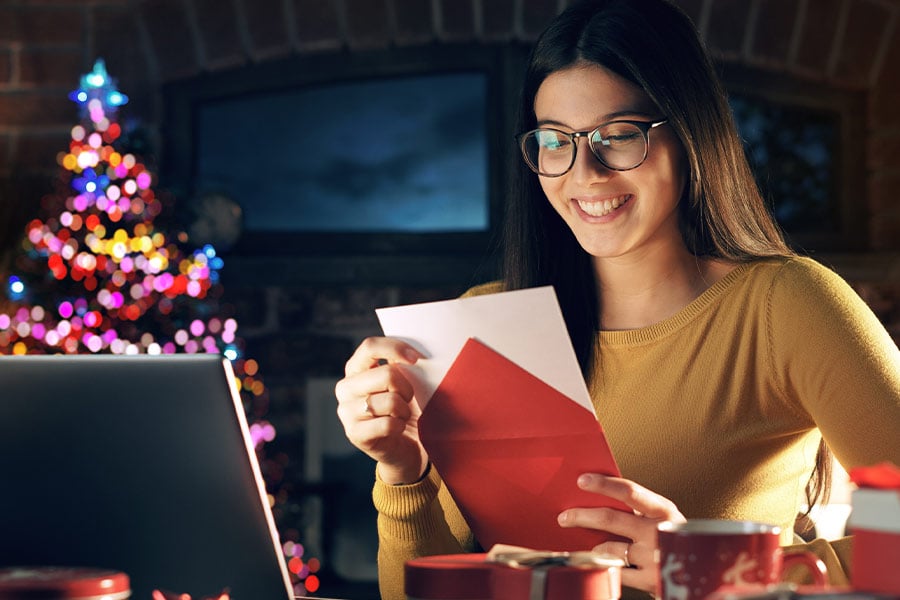 A smiling young woman with glasses opening a Christmas card