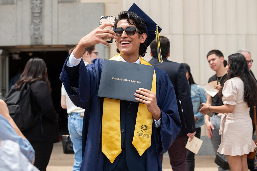 Graduate Victor Andrade uses his phone for social media as he smiles and poses with his diploma cover after the commencement ceremony for Cristo Rey Fort Worth College Prep, on Saturday, June 04, 2022 at Will Rogers Auditorium in Fort Worth. (NTC/Ben Torres)