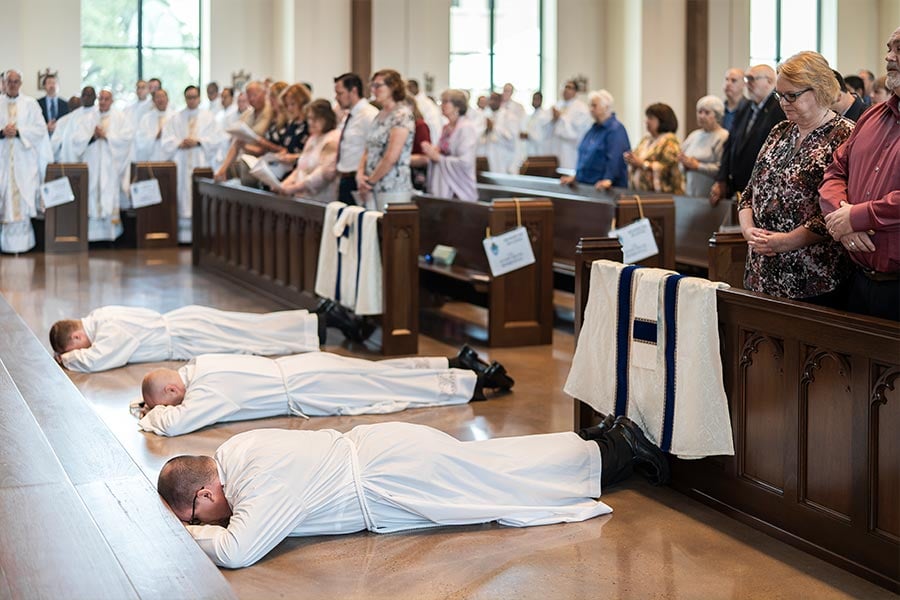 The three diaconal candidates lie prostrate during the Litany of Saints at the ordination Mass on May 21, 2022 at St. Philip the Apostle Church. (NTC/Juan Guajardo)