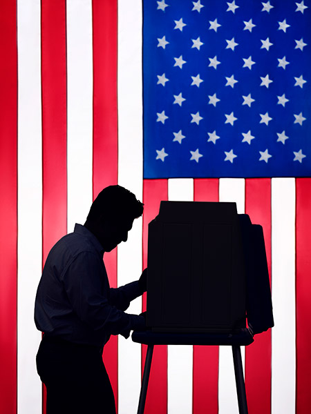 The silhouette of a person voting with the American flag in background.