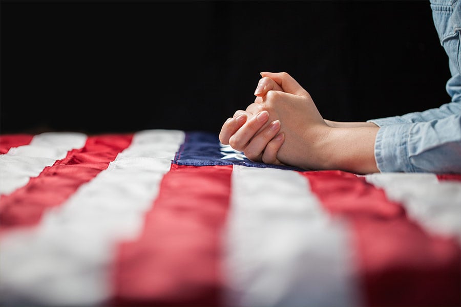 Folded hands resting on an American flag.