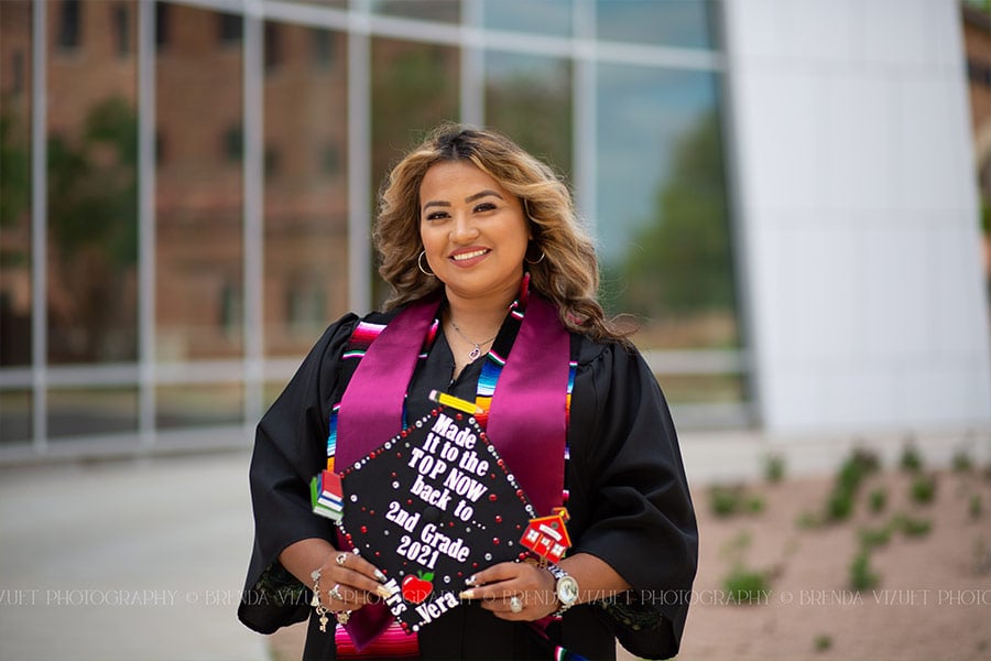 A young woman in a graduation gown holding her cap and smiling. (Copyright Brenda Vizuet)