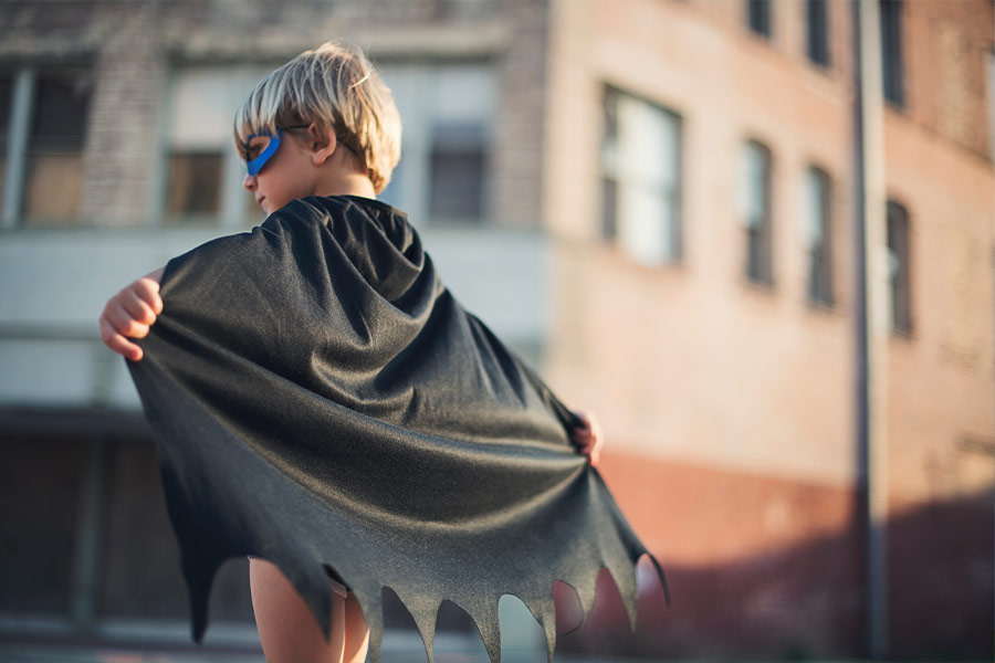 A boy dressed in a Batman costume spreading his cape