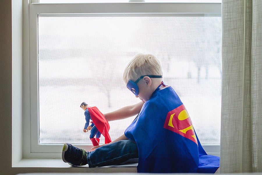 A boy dressed in a Superman costume playing with Superman figurine