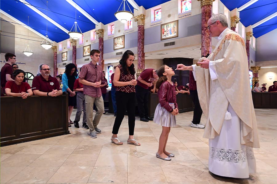 Kayla Lankford, 7, receives communion from Fr. James Flynn during the first annual Maroon Mass for Catholic Aggies, at St. Elizabeth Ann Seton Catholic Church in Keller, on May 27, 2022. Kayla's brother Leon Lankford, 16, fourth from right, attends Texas A&M. (NTC/Ben Torres)