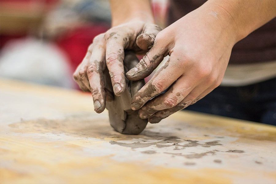 A close-up of hands molding a ball of clay on a table. (Unsplash.com/Alex Jones)