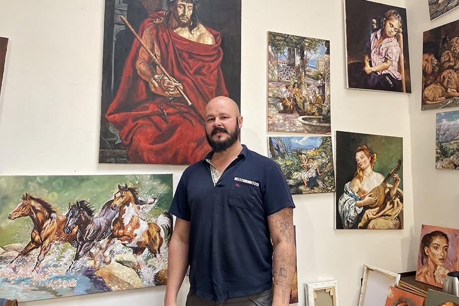 Adam Piekarski stands in front of his paintings in his studio at Palazzo Migliori, the Vatican's homeless shelter, Dec. 1, 2021. Piekarski, a homeless man from Poland currently living in Rome, was commissioned to paint images for the Vatican's 2021 Christmas stamps. (CNS photo/Junno Arocho Esteves)