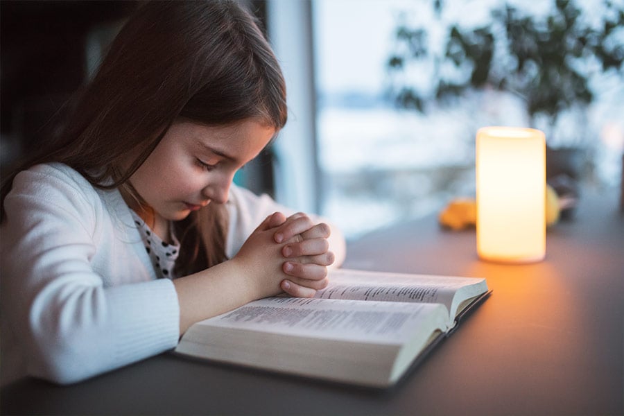 A small girl with bible at home, praying. (iStock)