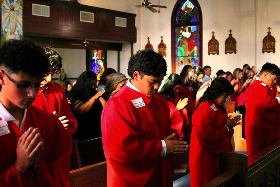 young adults draped in red robes praying during their confirmation Mass