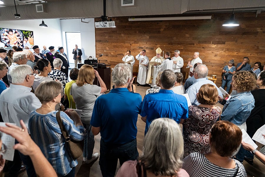 crowd of people make the sign of the cross as Bishop blesses the new formation center