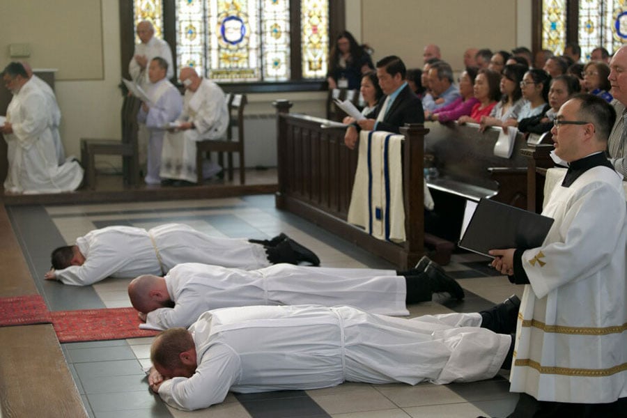 Trent Barton, Paul Trinh y Jeffrey Ambreit Jr. yacen postrados mientras el obispo y la congregación oran por ellos durante su ordenación al diaconado transitorio el 18 de marzo de 2026 en la Iglesia de Santa María de la Asunción en Fort Worth. (NTC/Juan Guajardo)