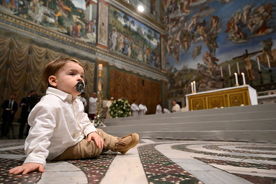 The older brother of one of 16 newly baptized infants sits on the floor during Pope Francis' celebration of Mass and the rite of baptism in the Sistine Chapel at the Vatican Jan. 7, 2024, the feast of the Baptism of the Lord. (CNS photo/Vatican Media)