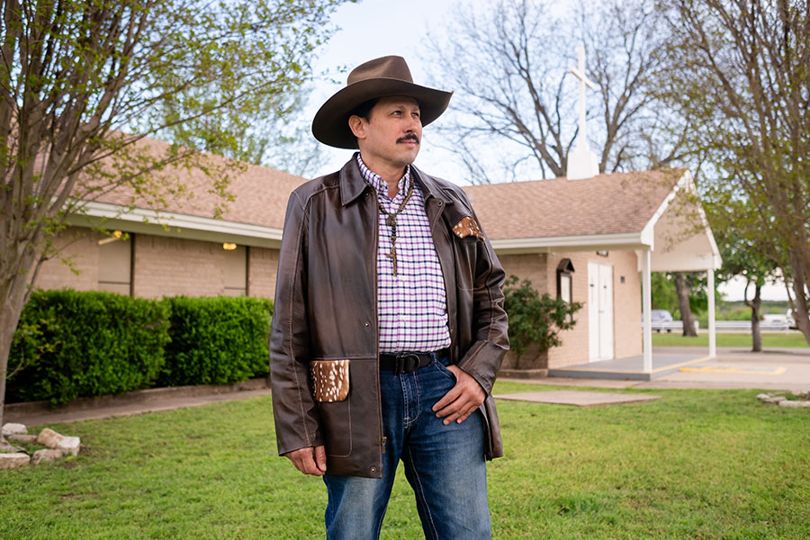 A man in a cowboy hat stands before a church