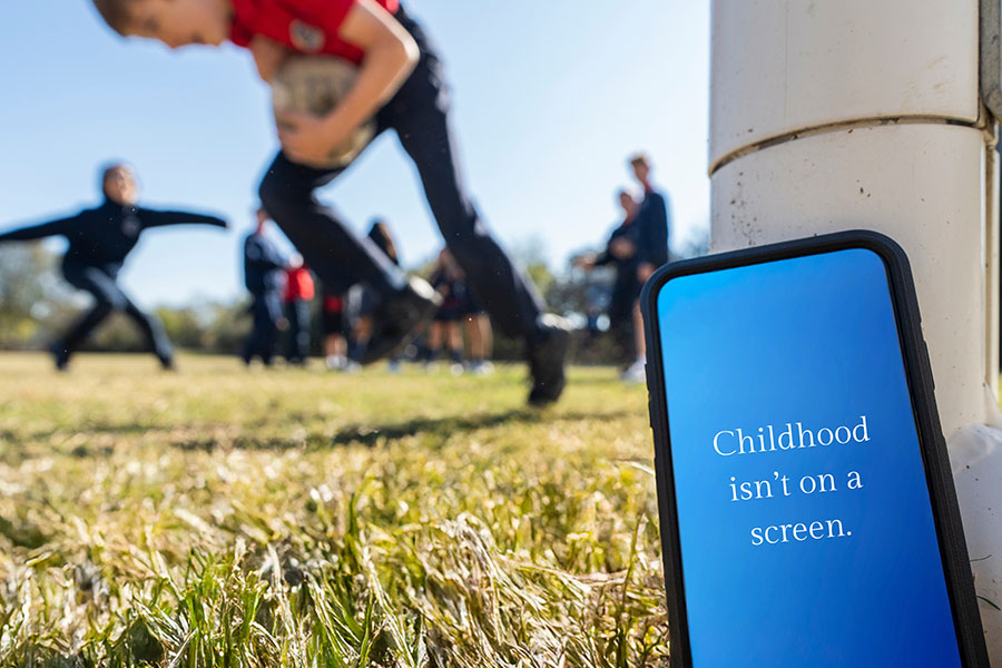 Kids play soccer; a phone, close up, reads "Childhood isn't on a screen."