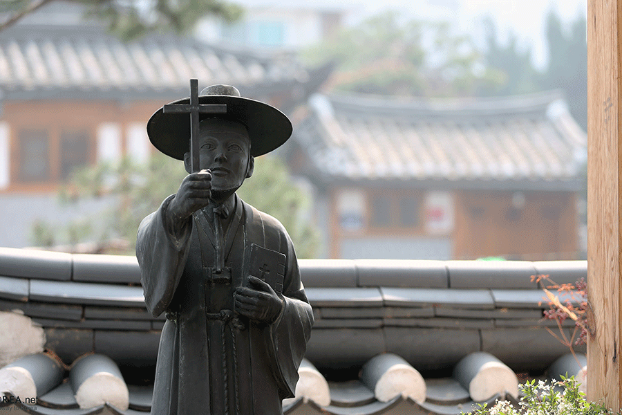 A statue of a Korean saint holding a bible and a cross