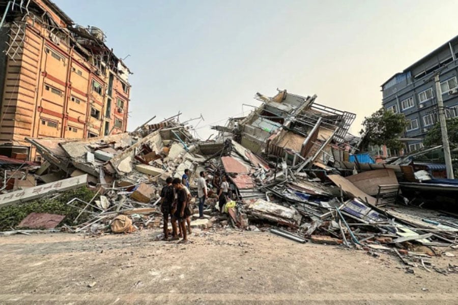 People stand past the debris of a collapsed building in Mandalay, Myanmar, on March 28, 2025, after a powerful earthquake killed more than 150 people across Myanmar and Thailand on March 28, toppling buildings and bridges and trapping over 80 workers in an under-construction skyscraper in Bangkok.
