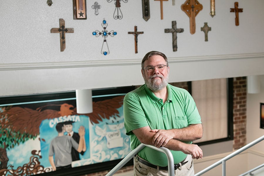Kenny Scagel stands before a mural of Cassata and collection of crucifixes