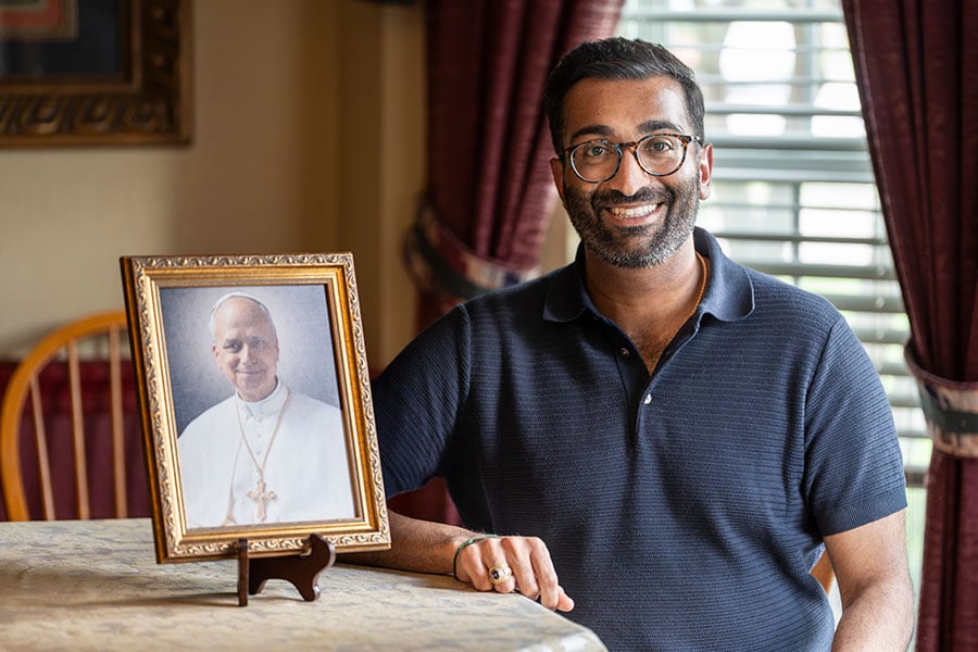 Devan Patel sits at a table next to a framed photo of Pope Leo XIV
